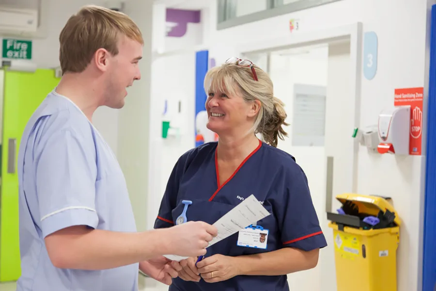 A nurse and a doctor speaking to each other on a ward