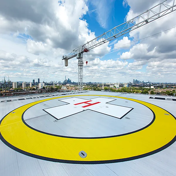 A birds-eye view of the helipad on a bright day with blue skies. There is a large yellow circle with a red cross in the middle to indicate where the landing strip is located for air ambulances. The London skyline is visible in the background.