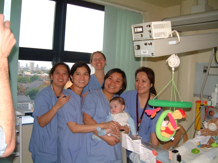 Reggie as a newborn baby, surrounded by 5 smiling nurses, with one in the middle holding him, in the children's ward at King's