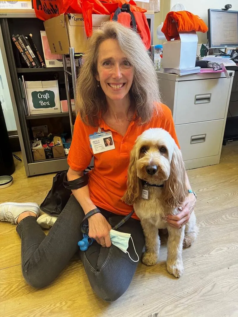 Photo of King's Volunteer Belinda sitting on the floor with therapy dog Maple looking at camera