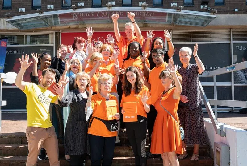 Photo of a group of about 20 volunteers standing in a huddle on steps and cheering with their hands in the air