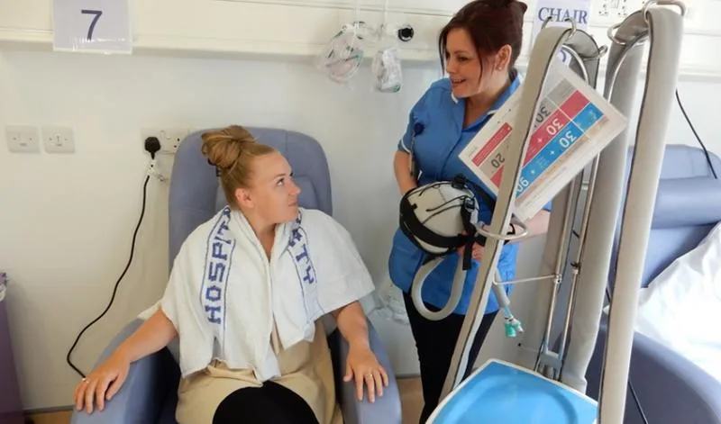 Picture of a woman sitting down with a nurse next to her holding a chemotherapy cap