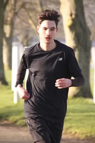 Reggie wearing all black running wear, running through the forest with the sun shining