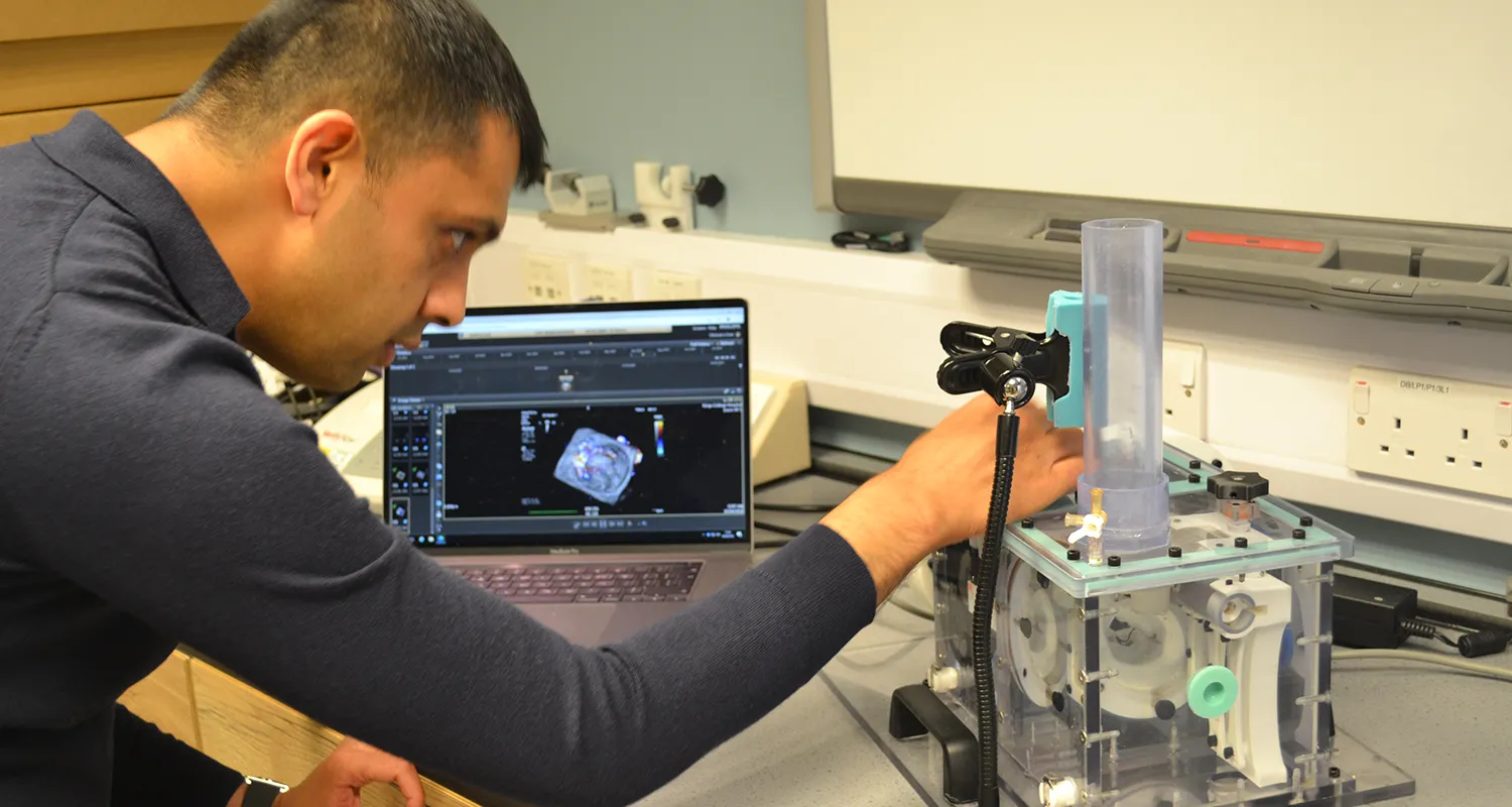 Dr Apu Bharucha in a clinical setting, leaning and operating the mitral valve simulator