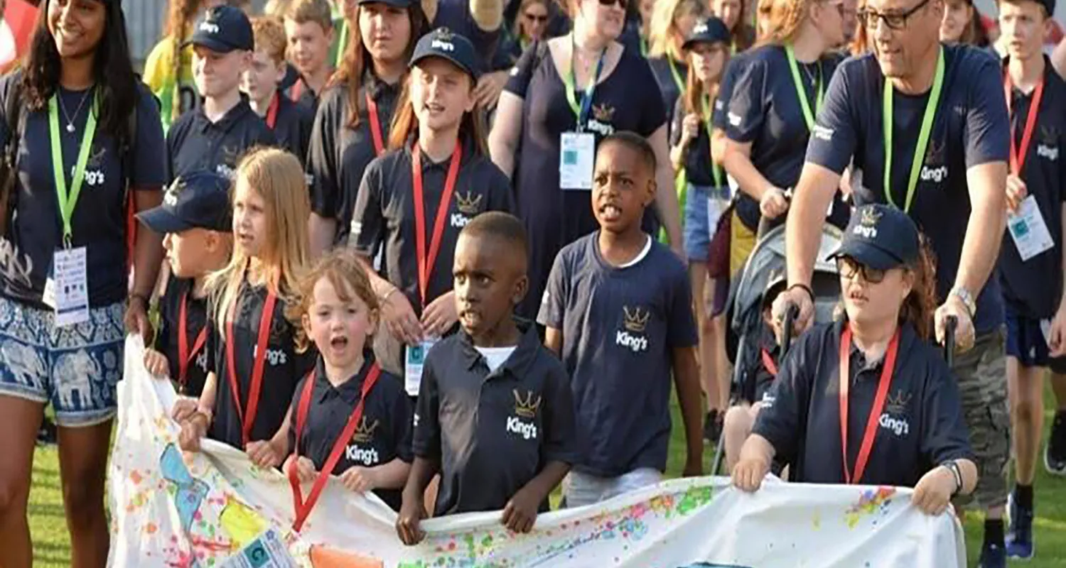 A group of 12 children and their mentors at the British Transplant Games, all wearing navy blue t-shirts and caps and holding a banner that reads 'Team King's'
