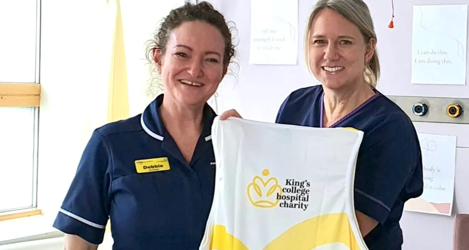 Two women (Debbie and Clare) in hospital scrubs holding up a King's College Hospital Charity running vest and smiling at the camera
