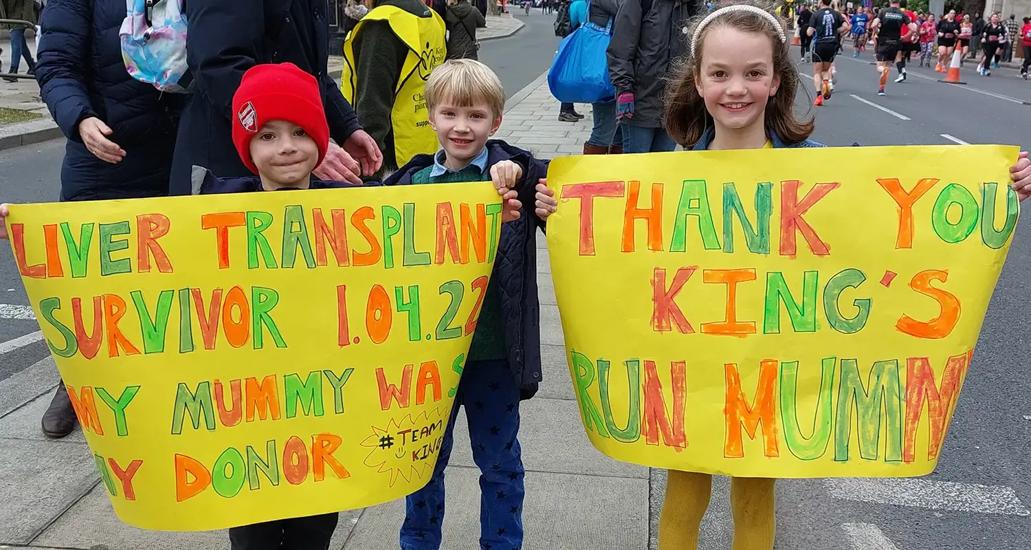 Photo of Georgeg and his sister holding up banners saying 'Liver Transplant Survivor - my mummy was my donor' and 'Thank you King's - RUN MUMMY!'