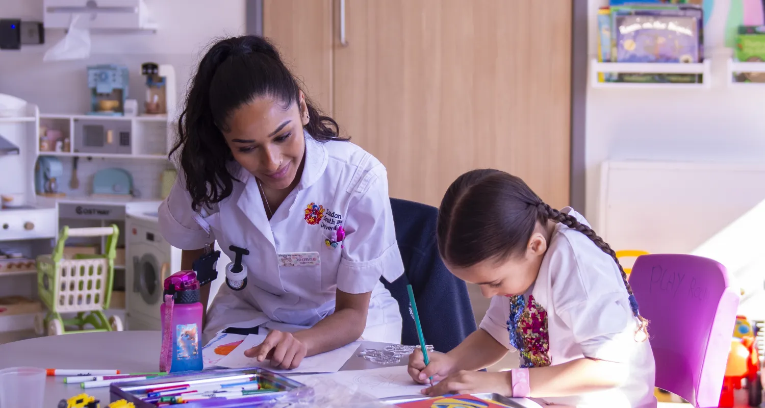 A nurse and child in a playroom, with colouring pens and books on a table