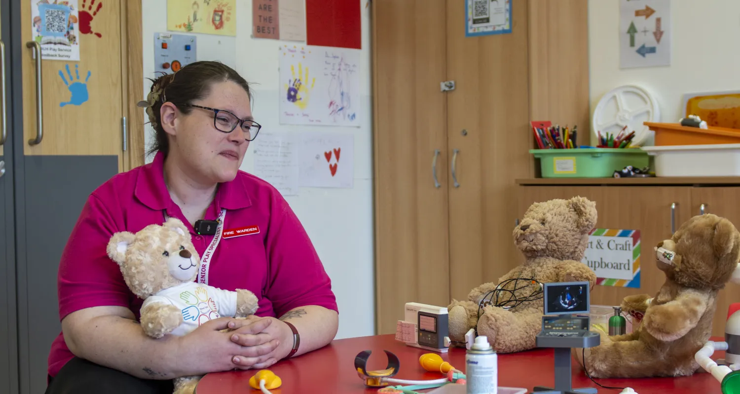 A healthcare play specialist seated at a table with soft toy teddy bears