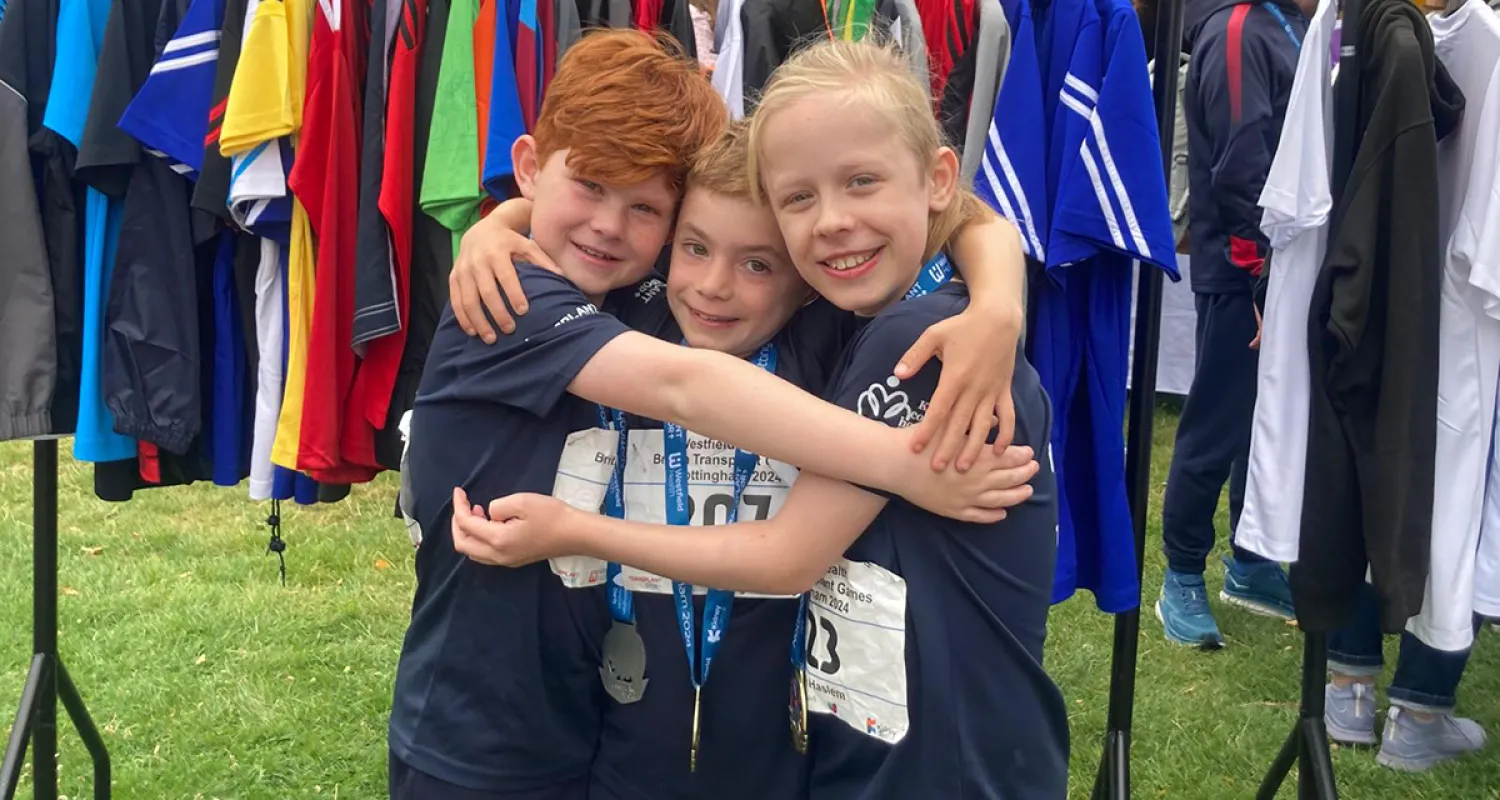 Three young boys in matching sportswear smiling and hugging wearing medals