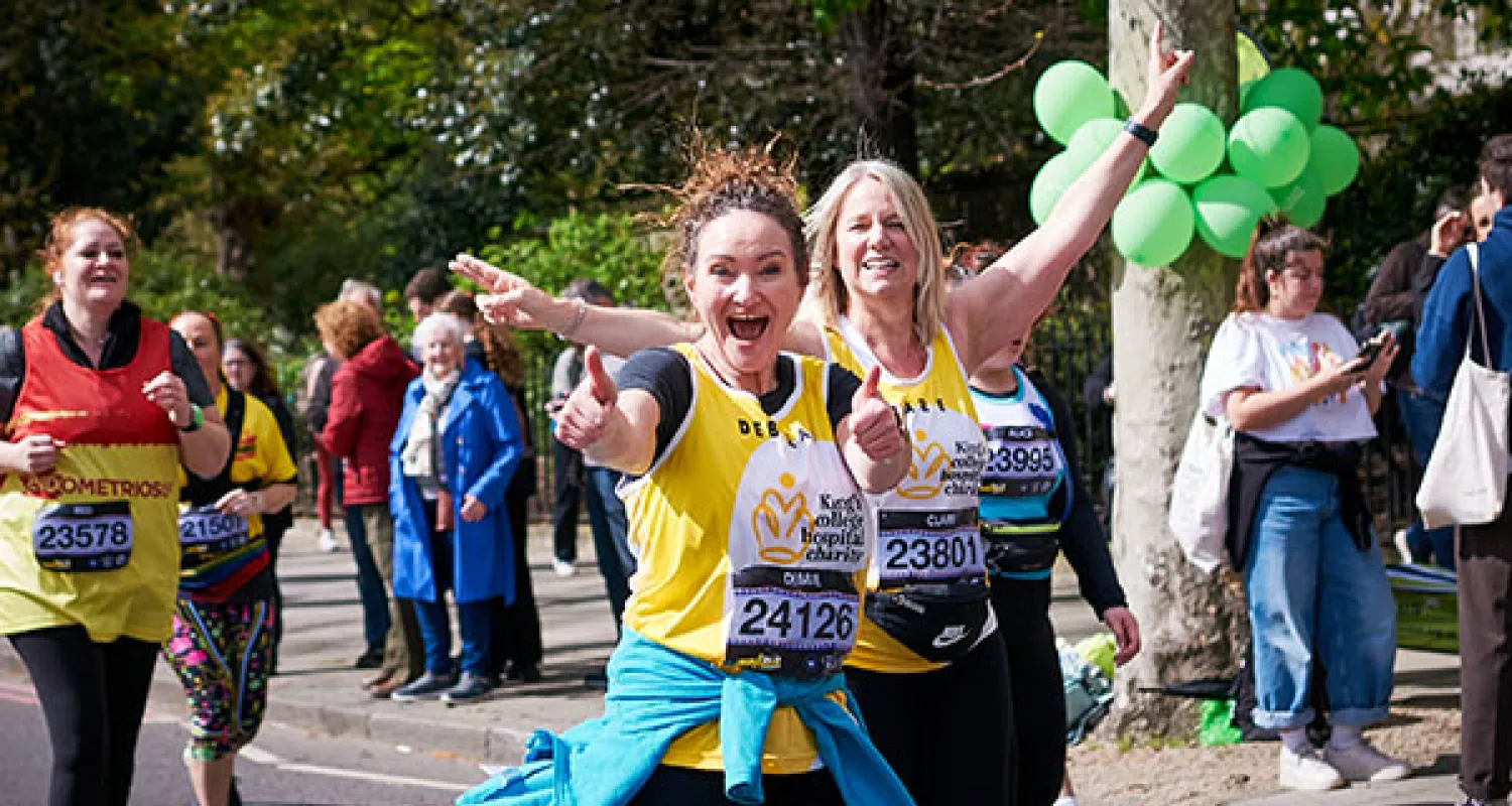 Two women in a King's College Hospital Charity running vest smiling at the camera and running in a race