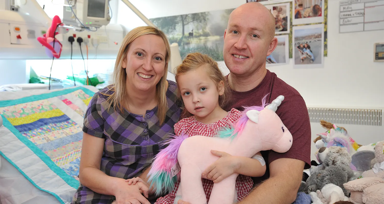 Photo of Molly with her family holding a unicorn teddy