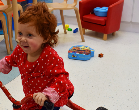 Photo of Emily riding a tricycle in the playroom