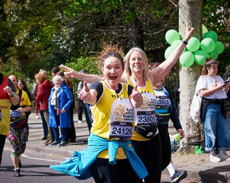 Two women in a King's College Hospital Charity running vest smiling at the camera and running in a race