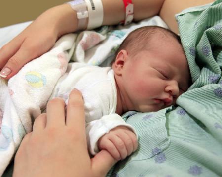 A newborn baby holding her mother's thumb