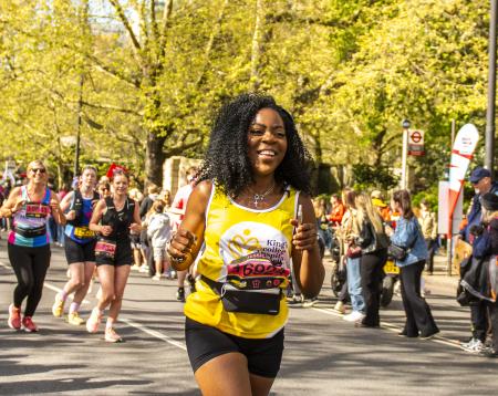 A lady in black shorts and King's running vest smiles as she runs 