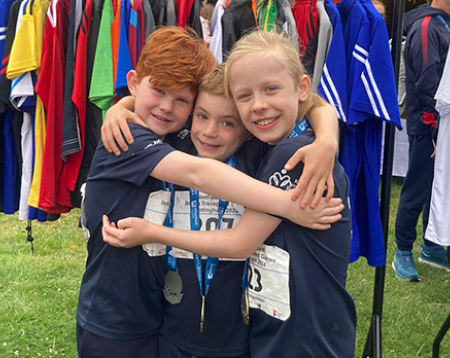 Three young boys in matching sportswear smiling and hugging wearing medals
