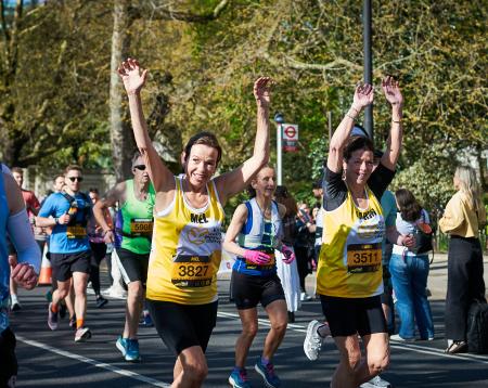 Two women wear yellow vests and run towards camera with their hands in the air