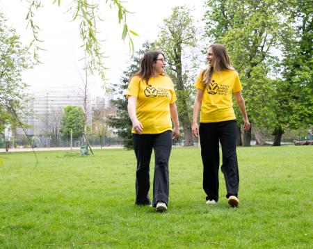 Two walkers in a park wearing yellow King's College Hospital Charity t-shirts
