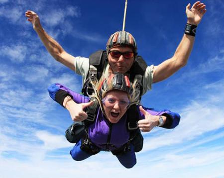 Photo of two people skydiving cheering with a blue sky behind them