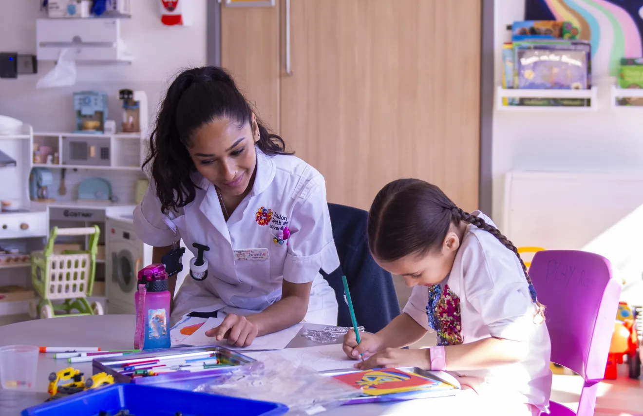 A nurse and child in a playroom, with colouring pens and books on a table