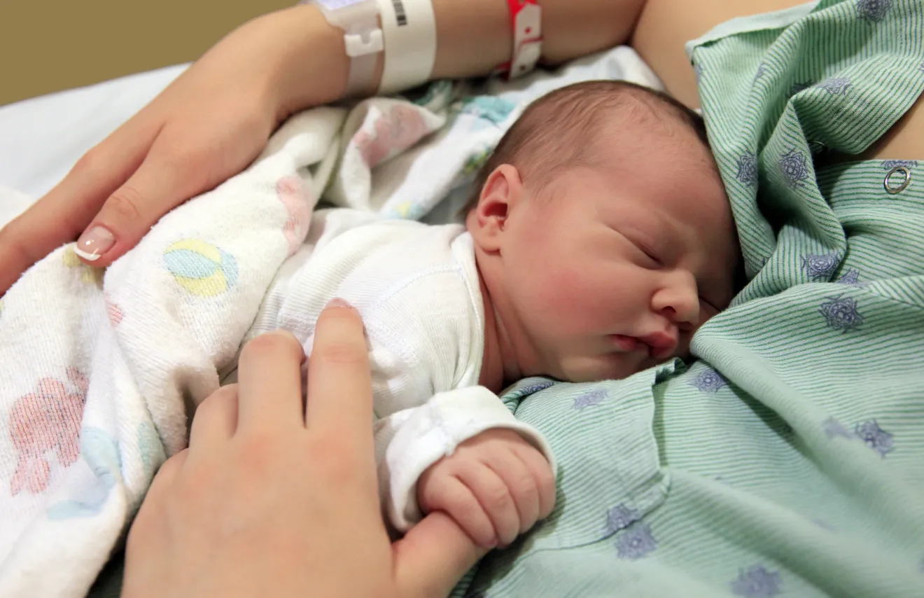 A newborn baby holding her mother's thumb