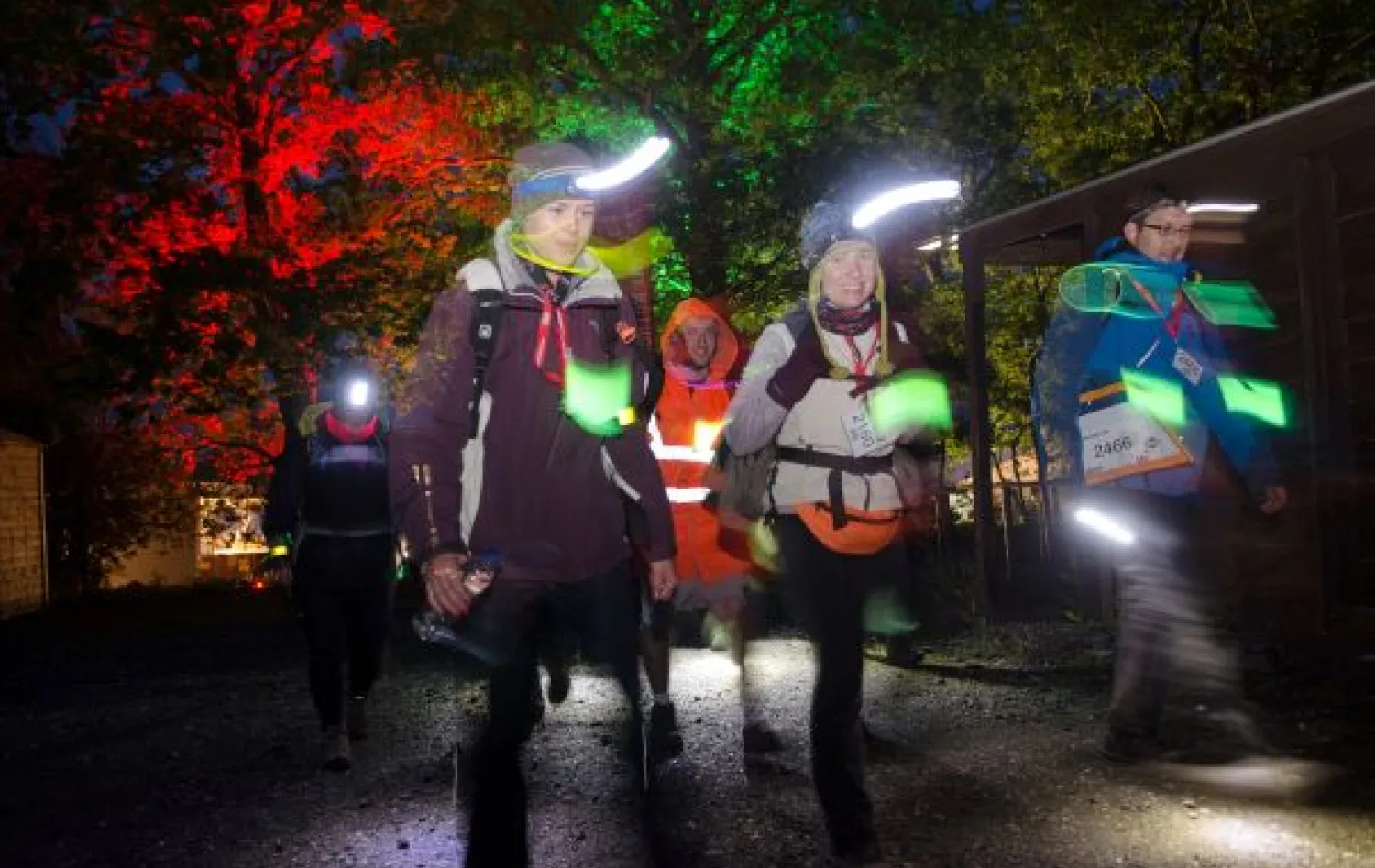 A group of people walk at night time, lit up with headtorches and other lights.