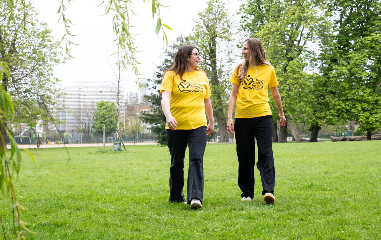 Two walkers in a park wearing yellow King's College Hospital Charity t-shirts
