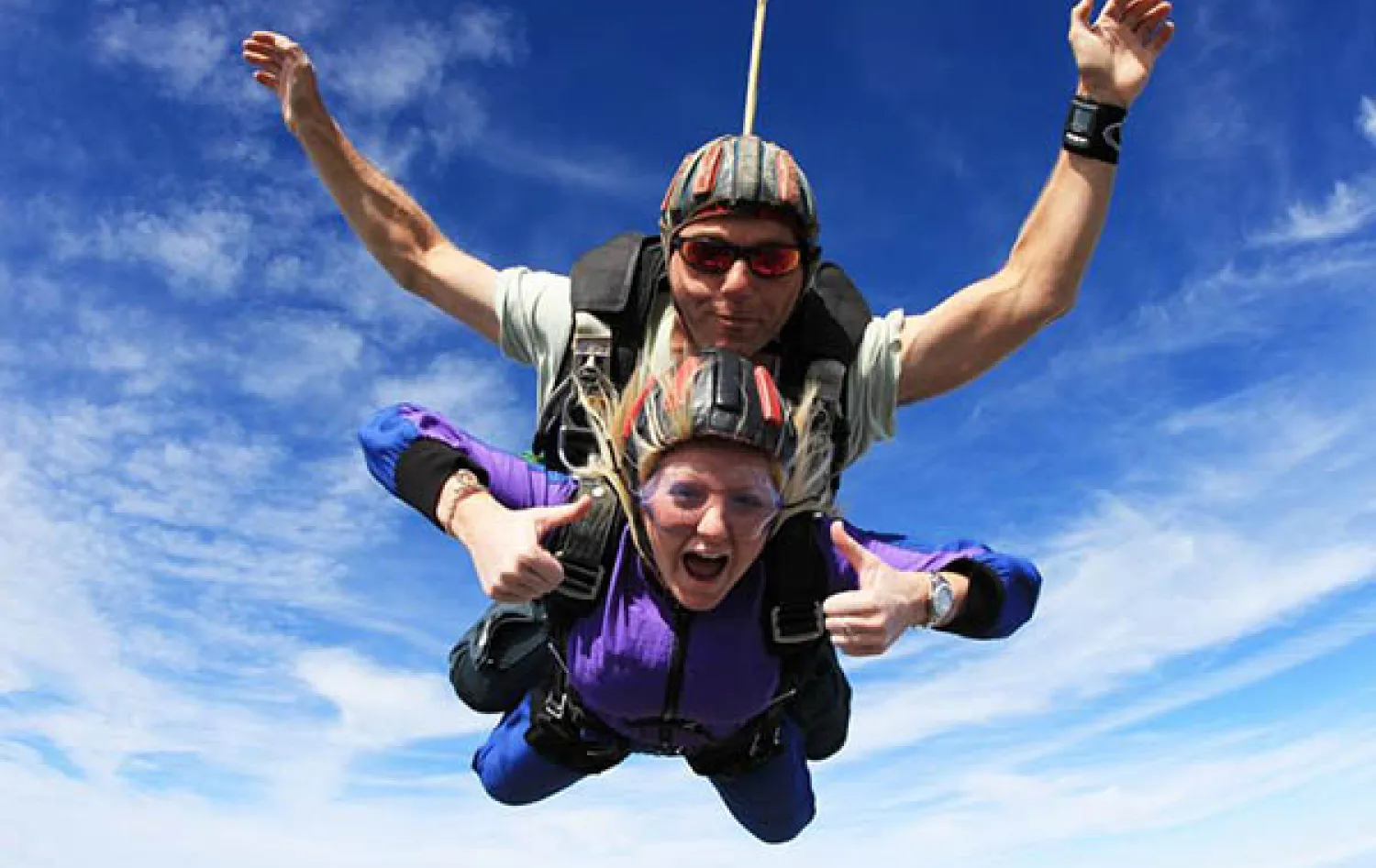 Photo of two people skydiving cheering with a blue sky behind them