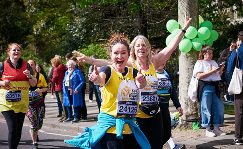 Two women in a King's College Hospital Charity running vest smiling at the camera and running in a race