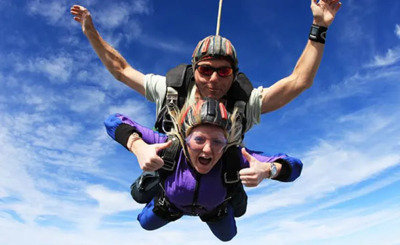Photo of two people skydiving cheering with a blue sky behind them