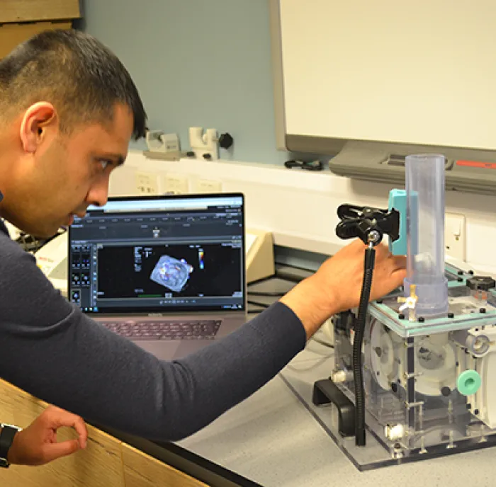 Dr Apu Bharucha, in a clinical setting leaning across the mitral valve simulator