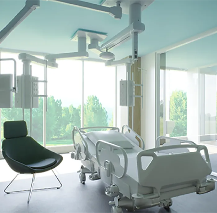 The new Critical Care Unit. It is a brightly lit patient room with large windows, with a view to Ruskin Park and many trees. There is a patient bed in the middle and a black visitor's chair on the left hand side.