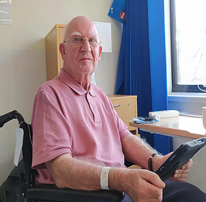 Brian, wearing a pink t-shirt, sitting in a wheelchair holding the patient entertainment system