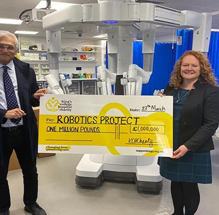 Gail Scott-Spicer (King's College Hospital Charity's CEO), and Musallam Al Akash, Consultant Colorectal Surgeon at King's, at the robot's unveiling. Gail and Musallam are standing in front of a giant robot and are holding a giant yellow charity cheque for £1 million.