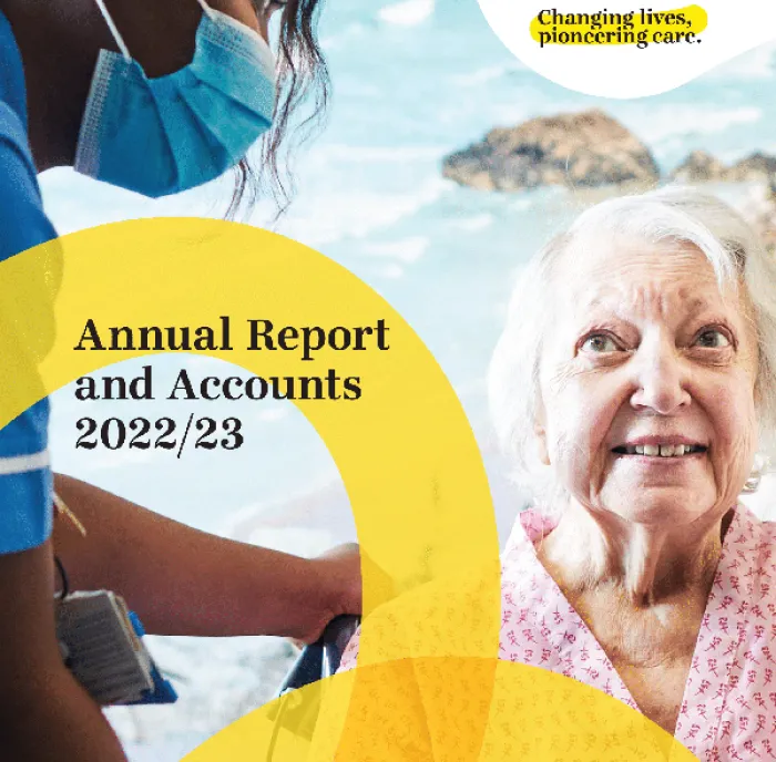 Picture of annual report front cover with nurse wearing mask while caring for elderly patient smiling with a picture of the sea in the background