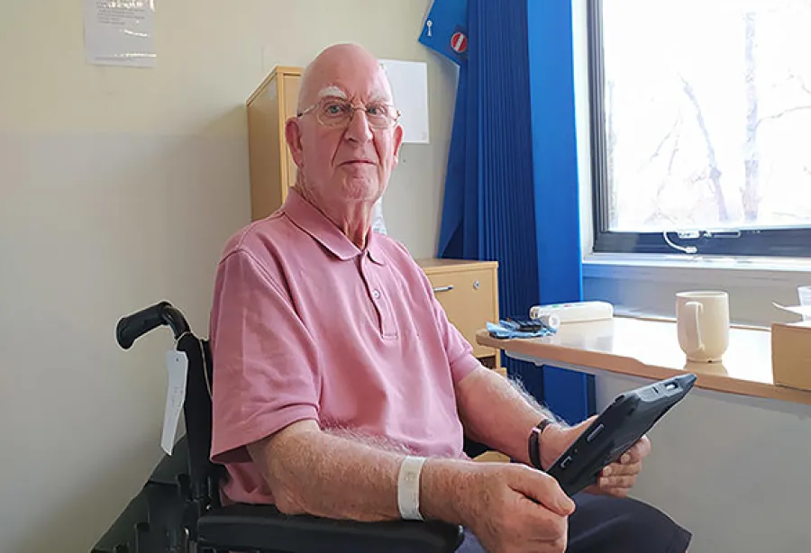 Brian, wearing a pink t-shirt, sitting in a wheelchair holding the patient entertainment system
