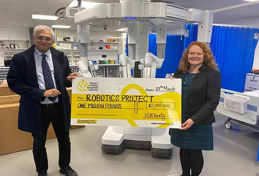 Gail Scott-Spicer (King's College Hospital Charity's CEO), and Musallam Al Akash, Consultant Colorectal Surgeon at King's, at the robot's unveiling. Gail and Musallam are standing in front of a giant robot and are holding a giant yellow charity cheque for £1 million.