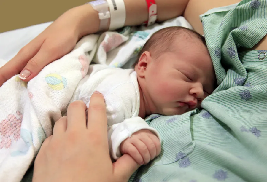A newborn baby holding her mother's thumb