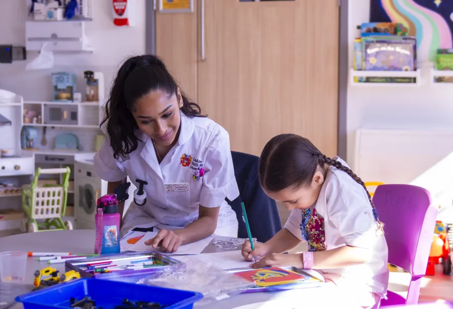 A nurse and child in a playroom, with colouring pens and books on a table