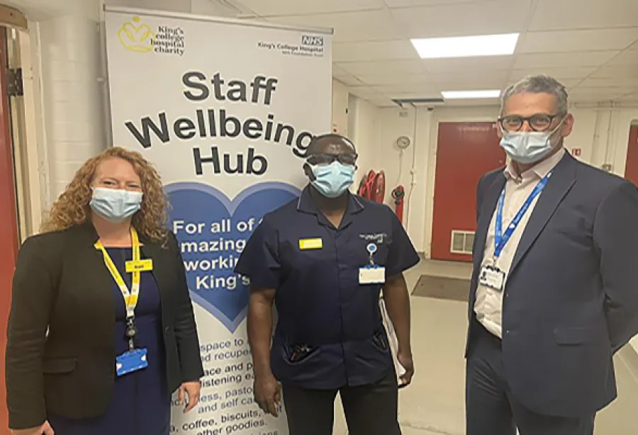 Gail Scott-Spicer (King's College Hospital Charity's CEO), and two King's staff members standing outside the Wellbeing Hub, all wearing masks. They are standing in front of a large banner in NHS-branded blue and white. The banner reads 'Staff Wellbeing Hub' and has a blue heart on it.