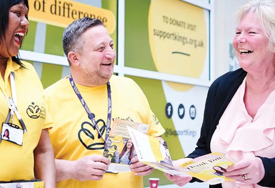 Picture of two fundraisers in yellow Charity t-shirts talking to a laughing supporter holding a Charity brochure