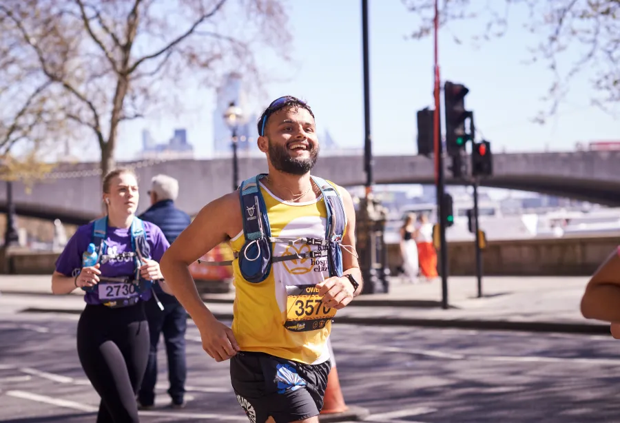 A man in a yellow vest jogs past camera smiling