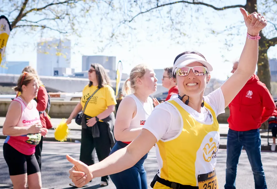 A lady in a  yellow vest is running and smiling broadly at someone off camera