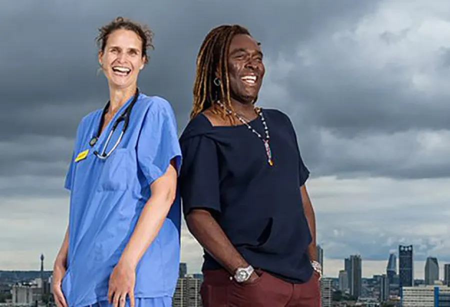 Picture of a doctor and patient standing back to back on helipad with cityscape and grey sky in background