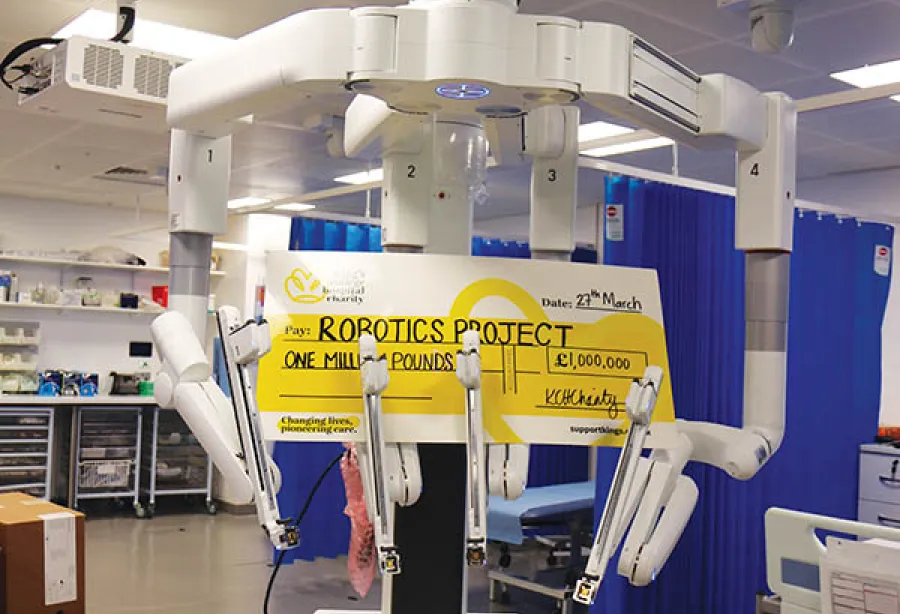 Picture of the surgical robot about 2.5m tall with four arms holding a cheque from the charity