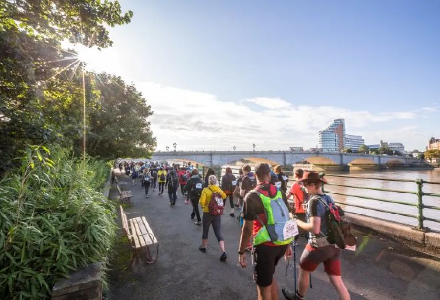 A group of walkers walk away from the camera with the Thames on their right.