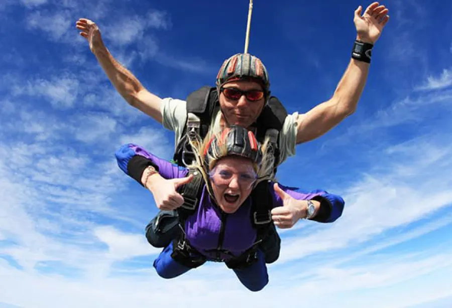 Photo of two people skydiving cheering with a blue sky behind them